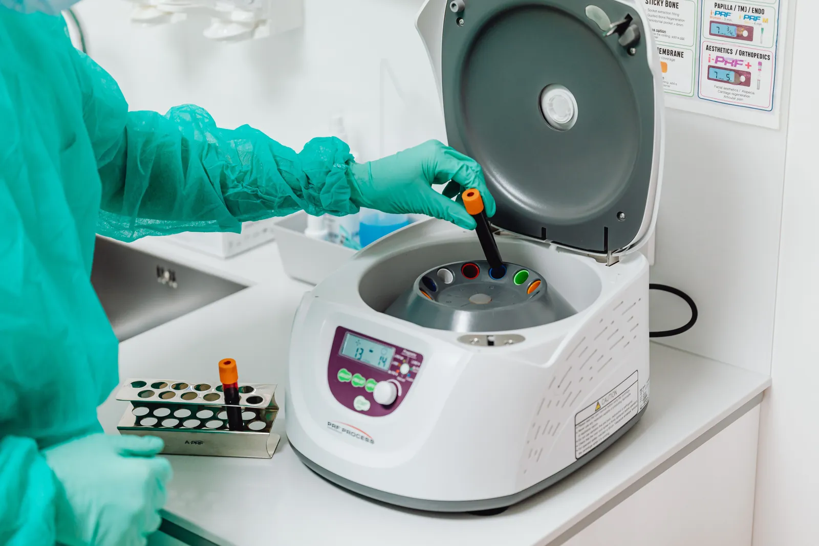 Laboratory technician in gloves and gown loading a blood collection tube into a centrifuge