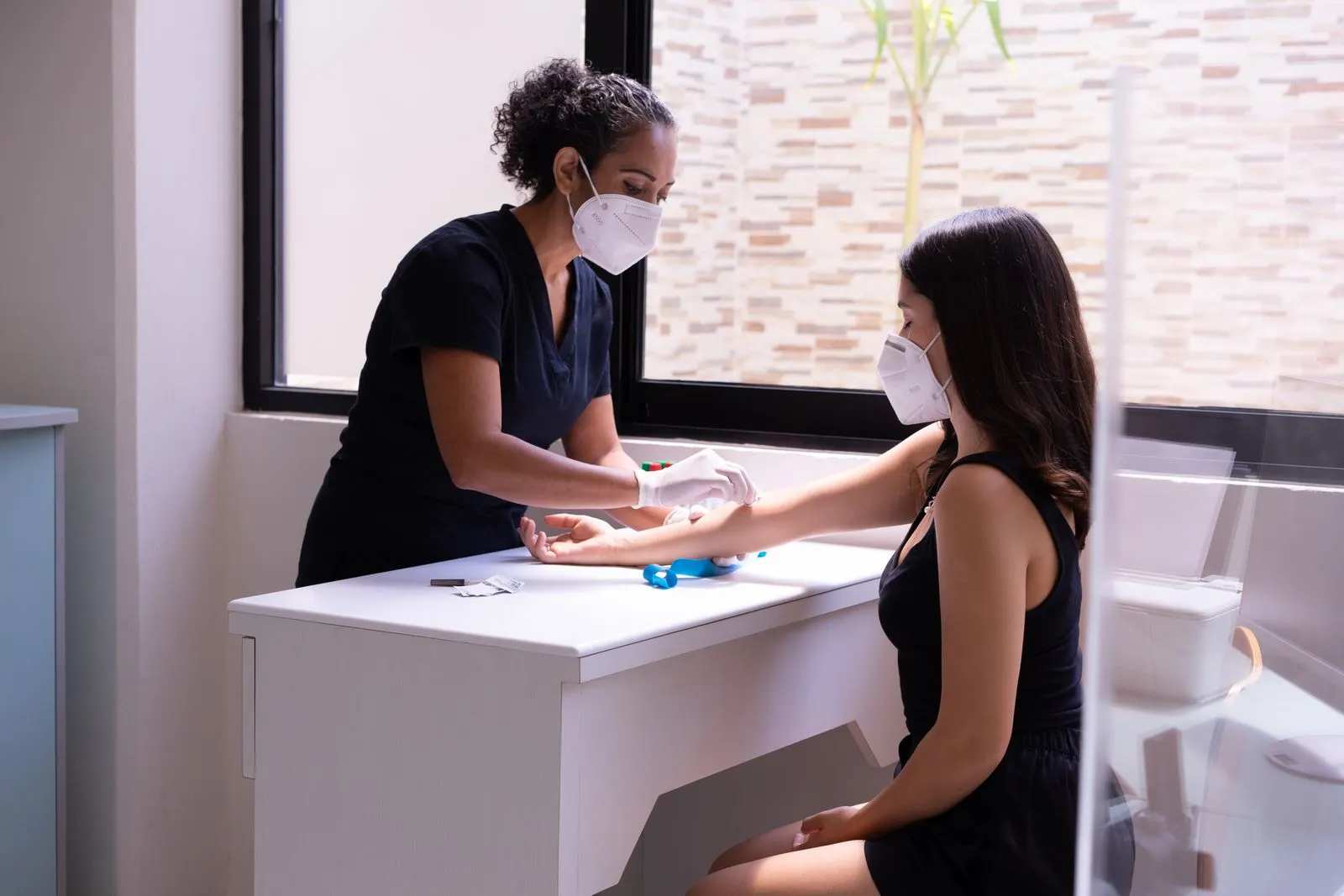 Mobile phlebotomist drawing blood from a seated patient in a bright clinic room